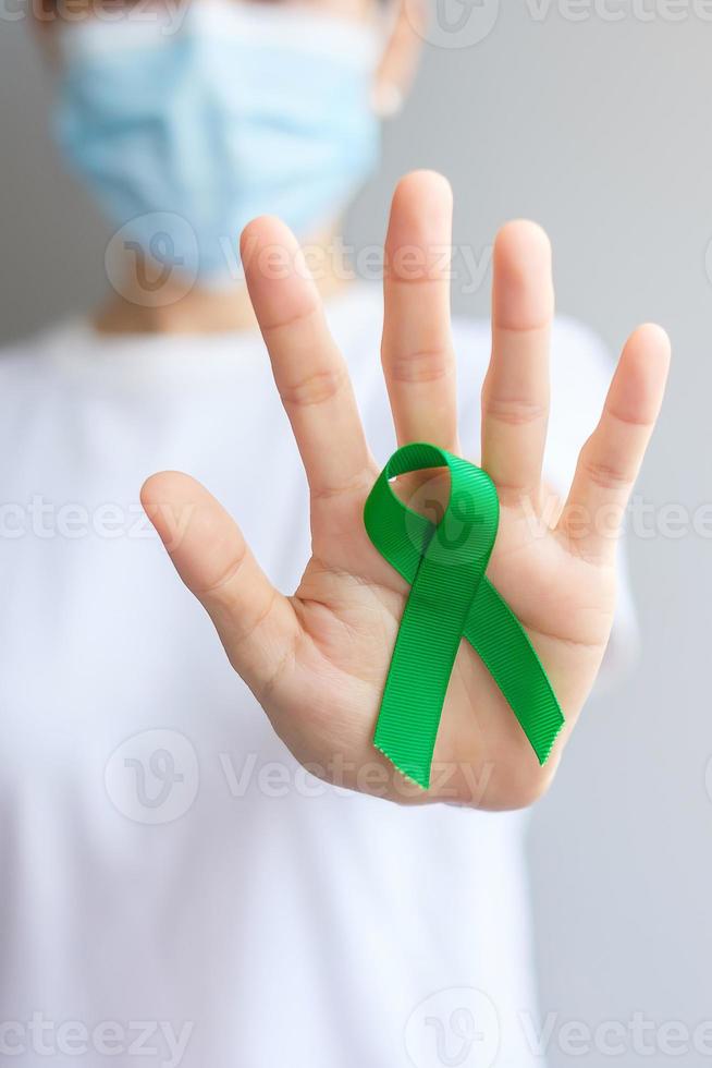 Hand holding green Ribbon for Liver, Gallbladders, bile duct, cervical, kidney Cancer and Lymphoma Awareness month. Healthcare and world cancer day concept photo