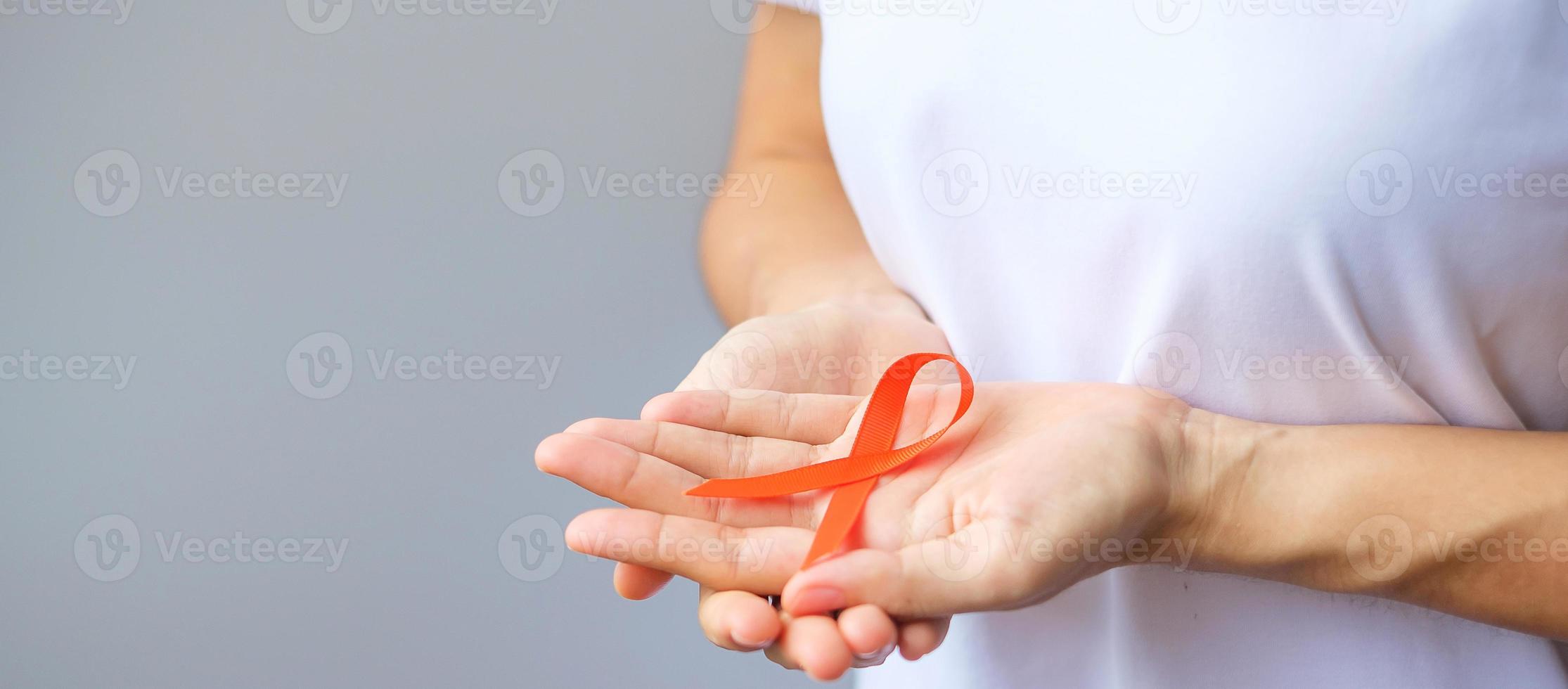 hand holding Orange Ribbon for Leukemia, Kidney cancer day, world Multiple Sclerosis, CRPS, Self Injury Awareness month. Healthcare and word cancer day concept photo