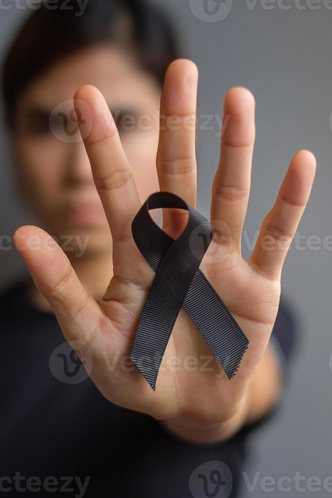 Woman holding black Ribbon for Melanoma and skin cancer, Vaccine injury awareness month, grief and rest in peace. Healthcare and Racist concept photo