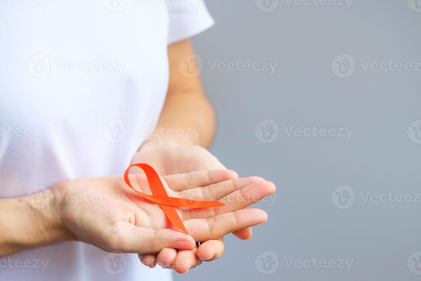 mano sosteniendo cinta naranja para leucemia, día del cáncer de riñón, esclerosis múltiple mundial, crps, mes de concientización sobre autolesiones. cuidado de la salud y el concepto del día del cáncer de palabra foto