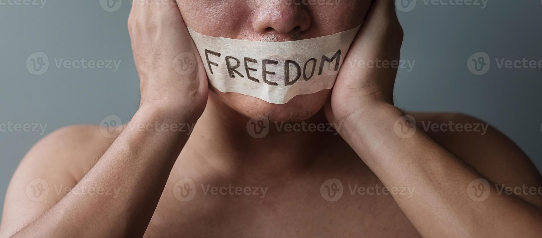Man with mouth sealed in adhesive tape with Freedom message. Free of speech, freedom of press, Human rights, Protest dictatorship, democracy, liberty, equality and fraternity concepts photo