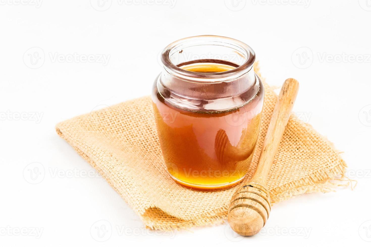Glass jar full of honey wooden honey dipper on white background photo