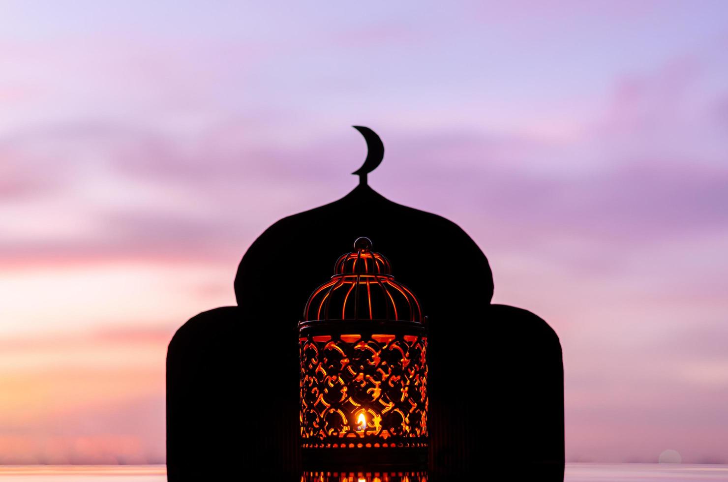 linterna con foco borroso de fondo de mezquita que tiene el símbolo de la luna en la parte superior y el cielo del amanecer. foto