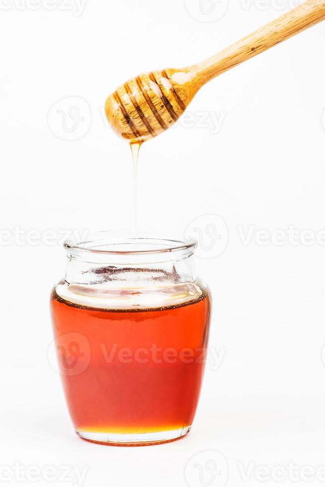 Glass jar full of honey wooden honey dipper on white background photo