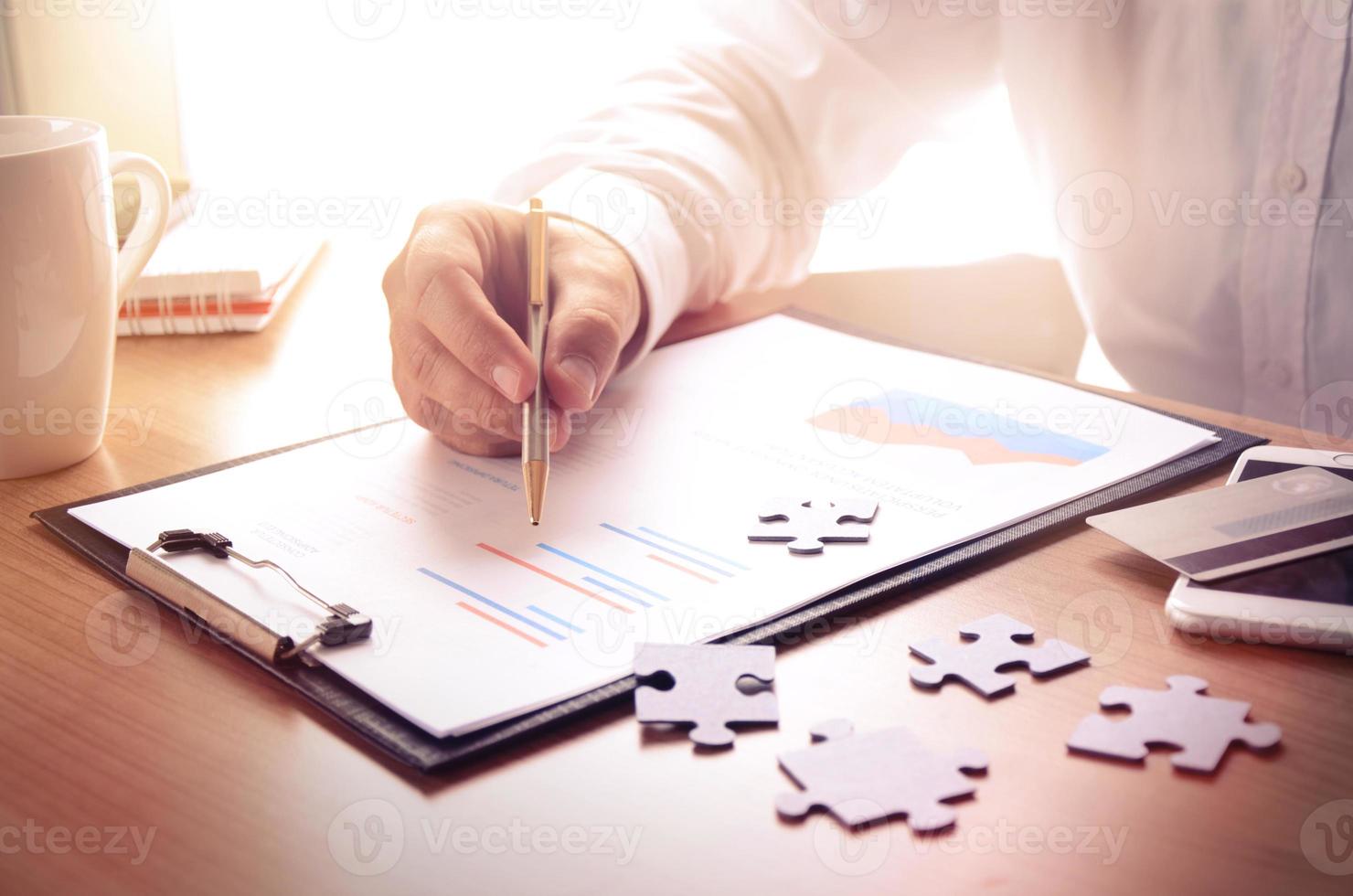 Businessman work with financial report at wooden office desk with puzzle pieces, smartphone, credit card and coffee cup. photo