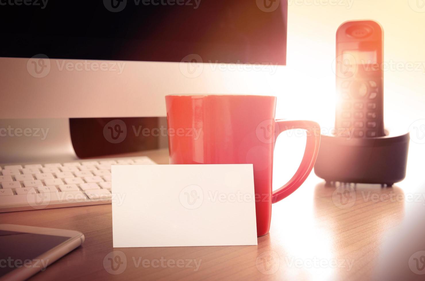 mesa de escritorio de oficina con teléfono inteligente, computadora, teléfono de escritorio, taza de café y tarjeta de presentación en blanco foto