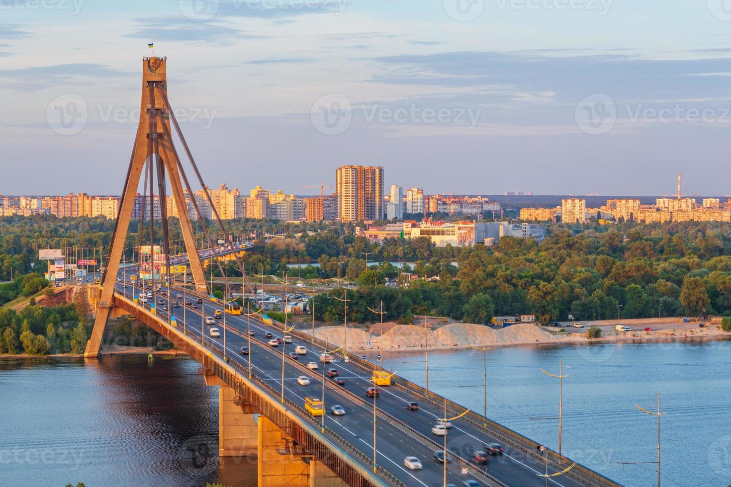 Light lines of passing cars on the North Bridge across the Dnieper River against a deep blue sky after sunset in Kyiv, Ukraine. photo