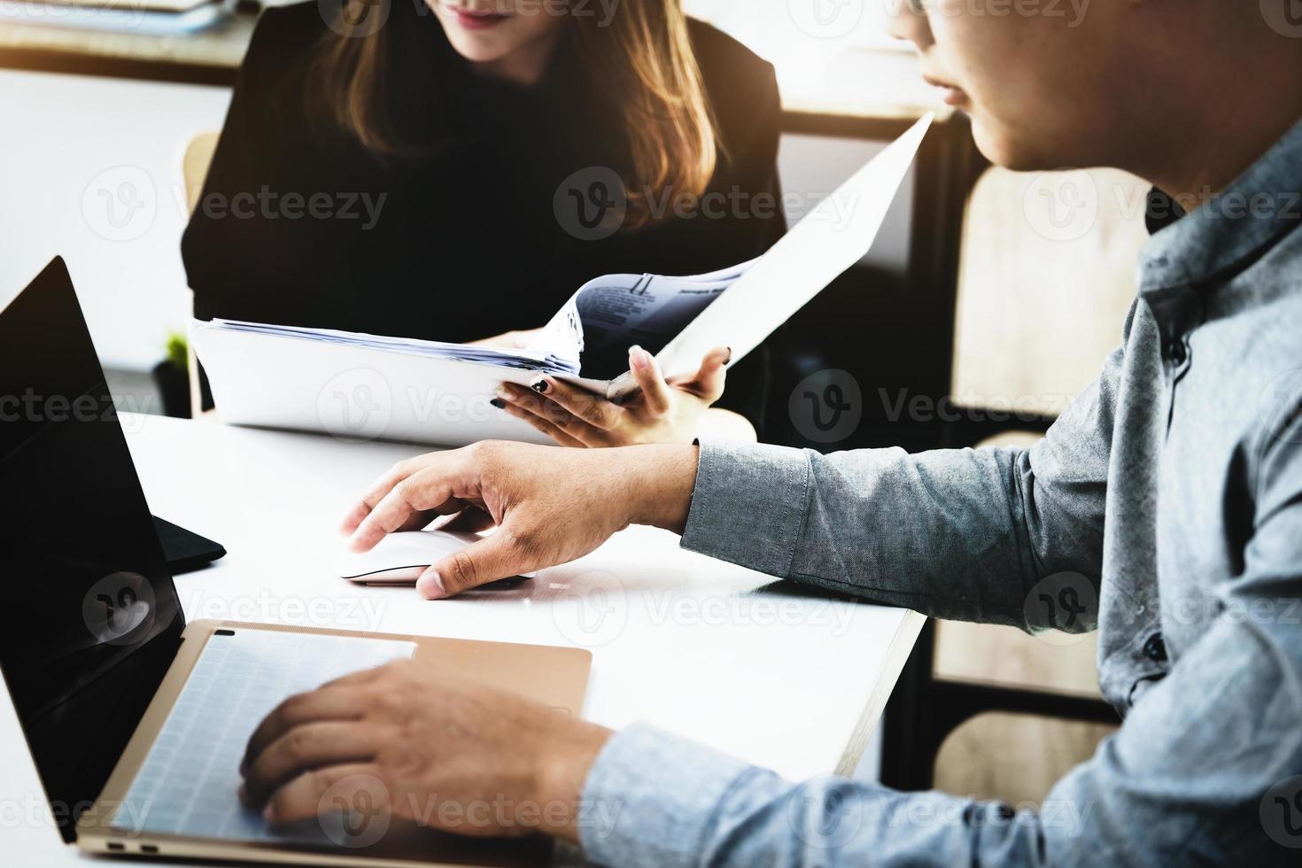 Focus on the male business owner using a computer mouse, while woman is browsing through the archives to find profitability information for the company. photo