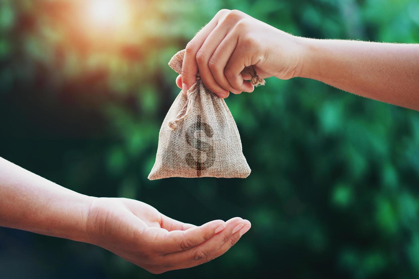 hand giving money bag to another people on green background with