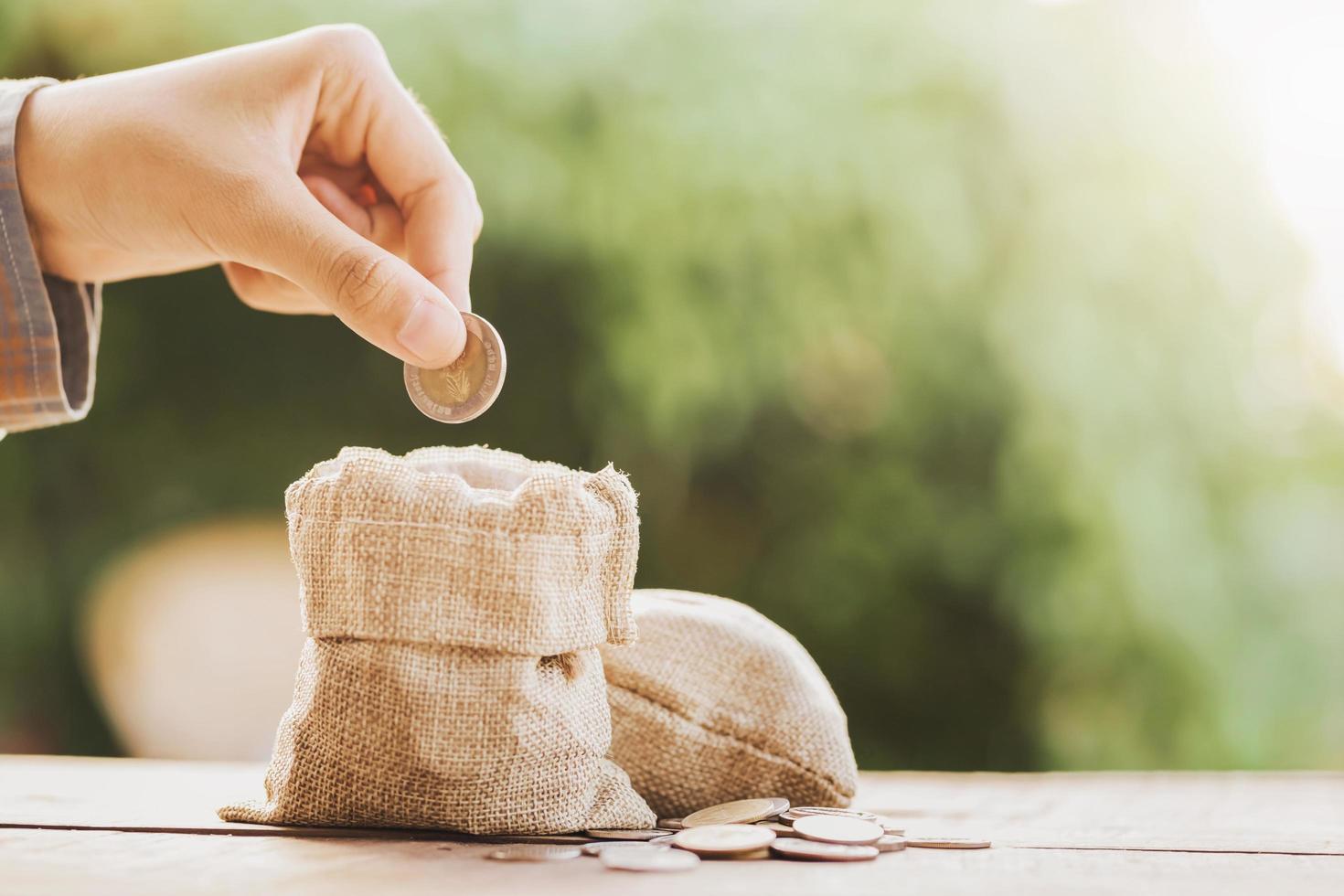 hand puting coins in money bag for saving on table background photo