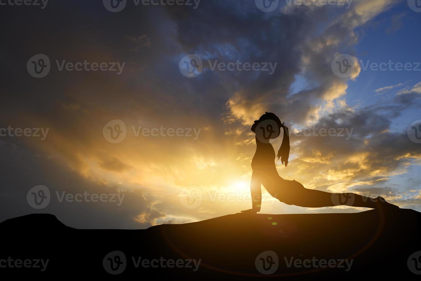 Silhouette young woman practicing yoga on the mountain at sunset. Meditation or exercise concept. photo