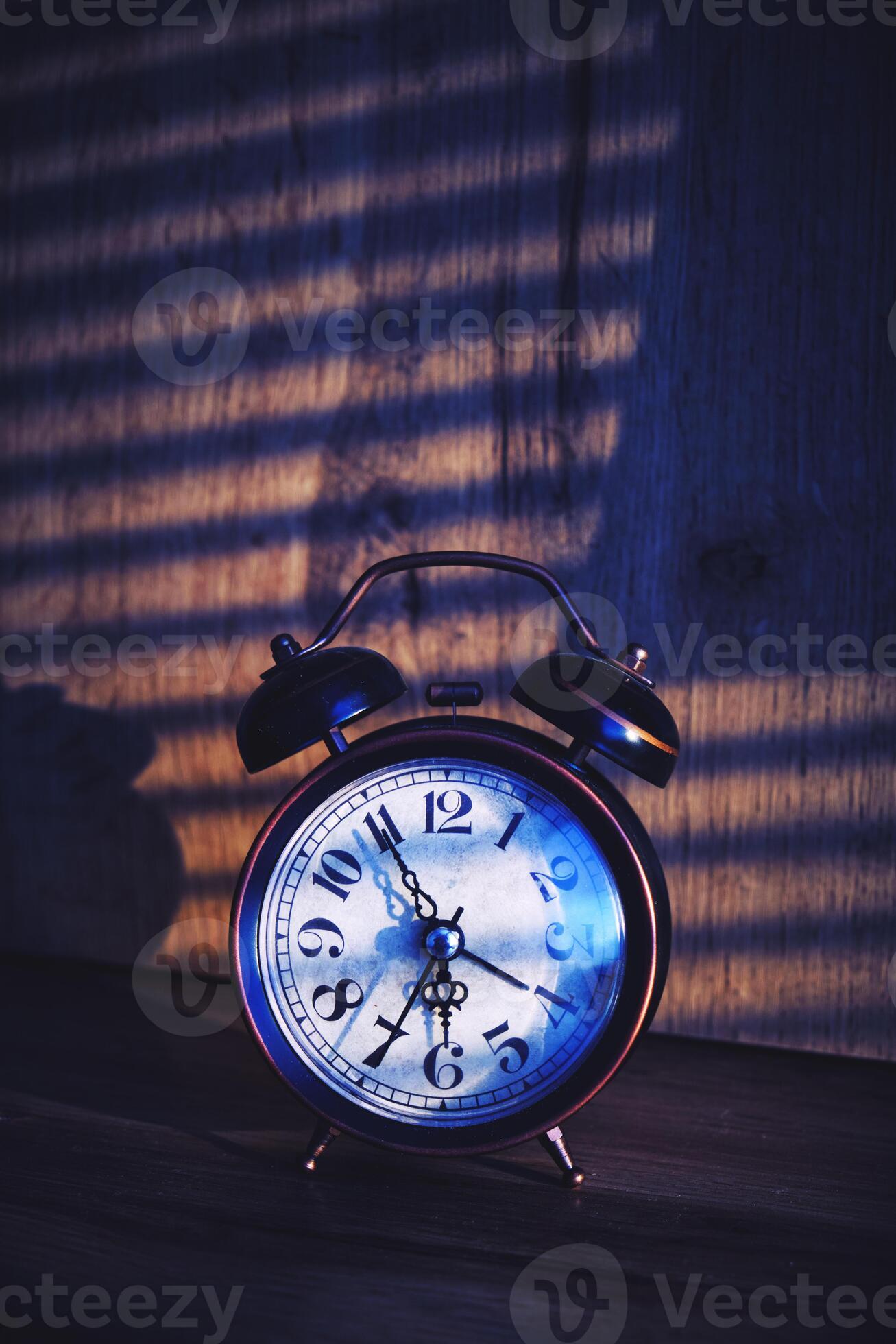 Retro alarm clock early morning on table rays sunlight through blinds