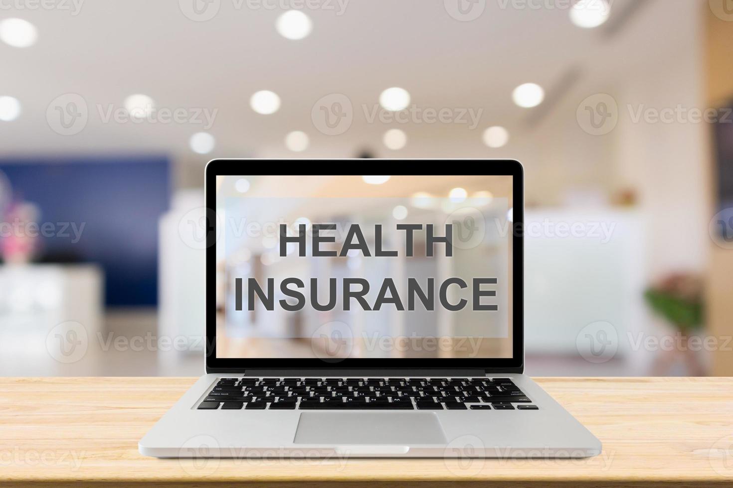 Laptop computer on wood table with Health Insurance text on screen with blur hospital room background healthcare concept photo