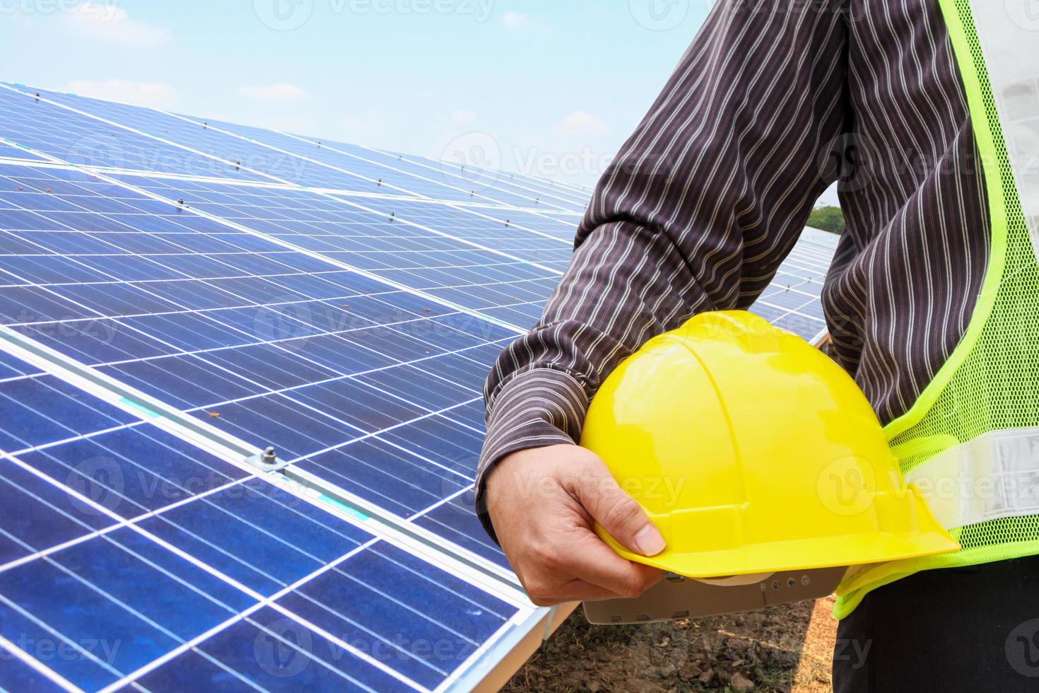 joven ingeniero de negocios tiene casco amarillo en el fondo del sitio de construcción de la planta de energía del panel solar foto