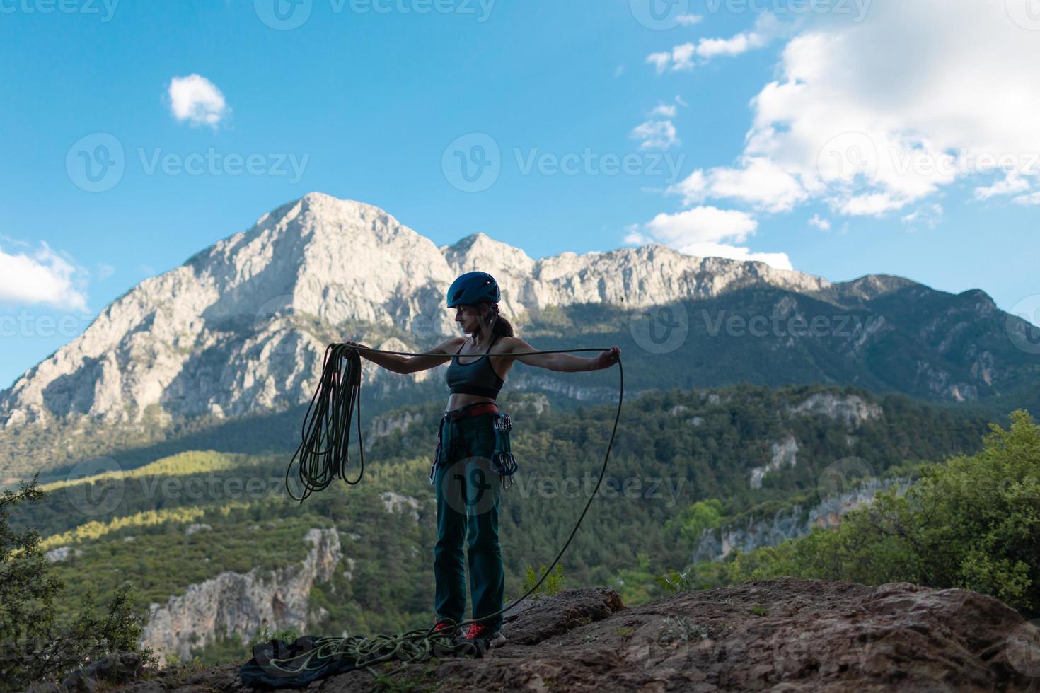 A woman in a helmet coils a rope against the background of a large mountain photo