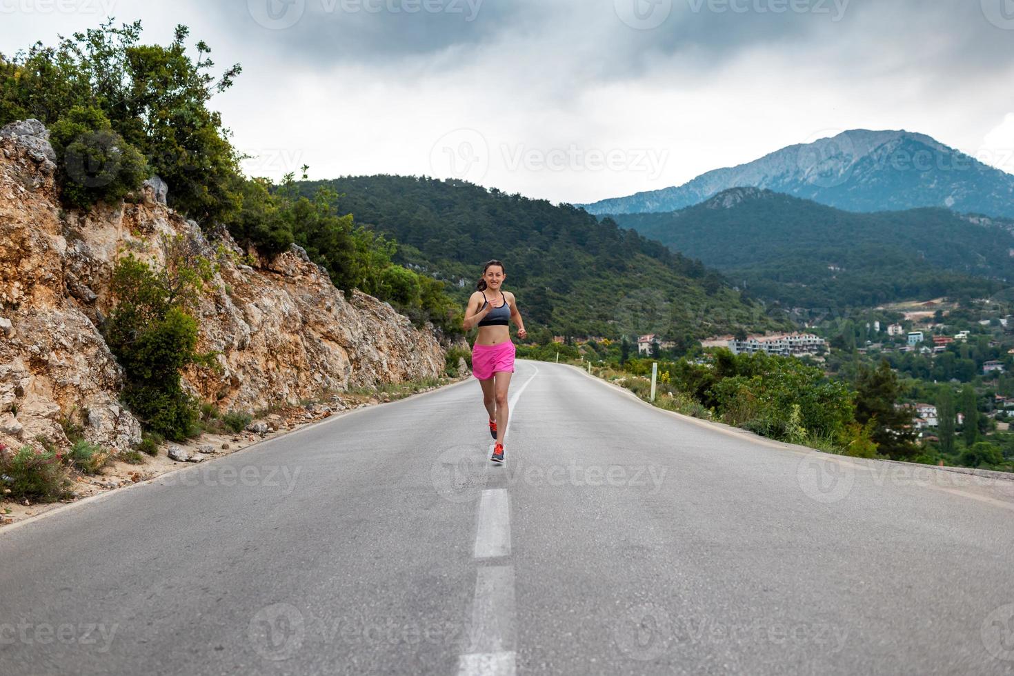 A girl runs along an asphalt road against the backdrop of beautiful mountains photo