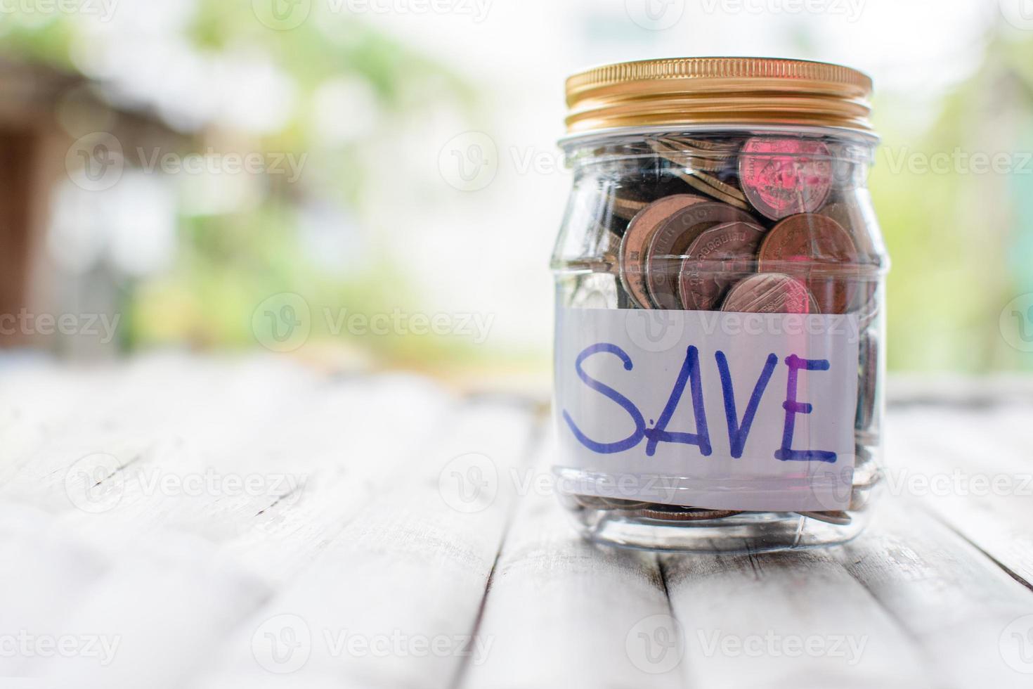 Coins and text SAVE in a glass jar placed on a wooden table. Concept of saving money for investment and emergency situations. Close up, Blurred background photo