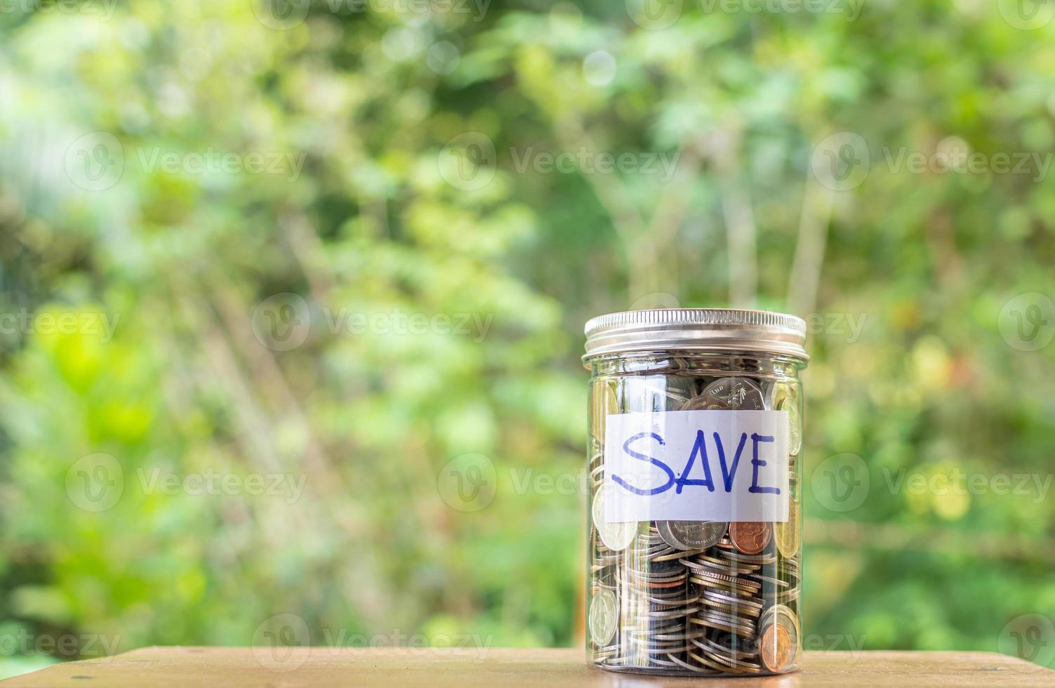 The coins and text SAVE in a glass jar placed on a wooden table. Concept of saving money for investment and emergency situations. Copy space top and left for content. Close up, Blurred background photo