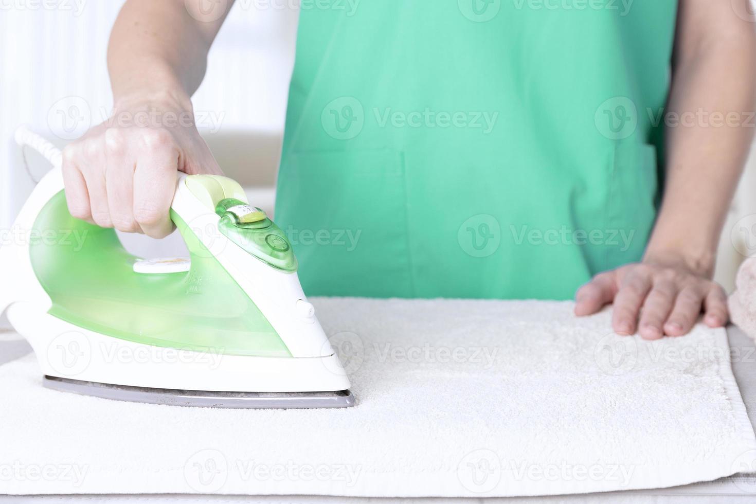 Caucasian woman, wife, mother, housewife, housekeeper, maid ironing linen with electric iron on ironing board. Home interior background. soft focus. photo