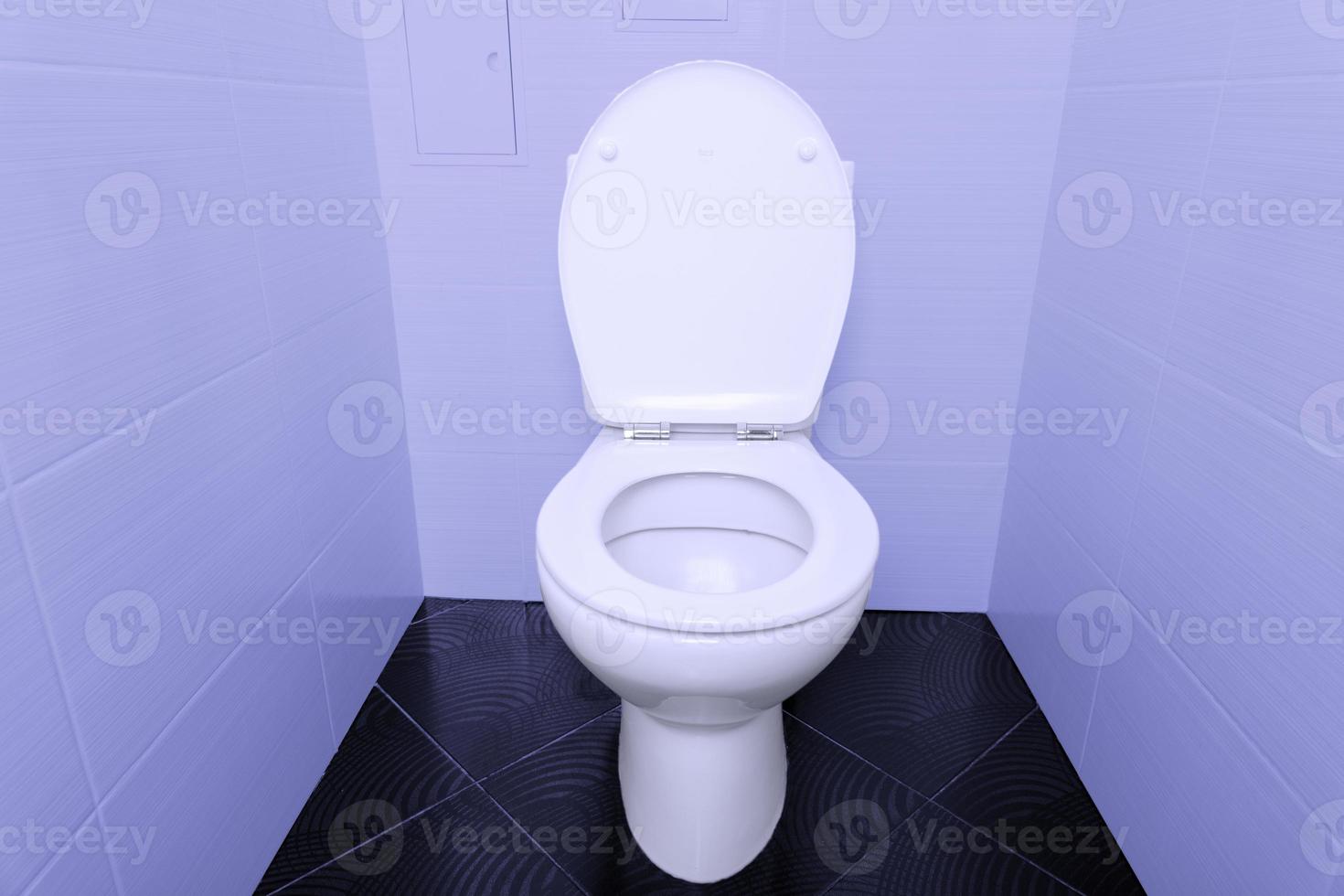 A white toilet bowl with an open lid on a black tiled floor and purple walls. photo