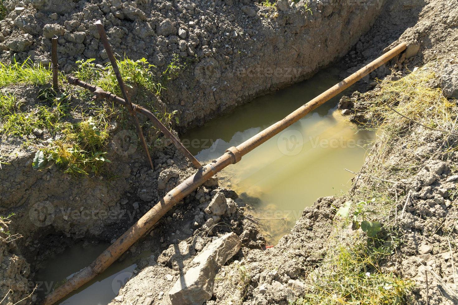 Old rusty metal pipes in a pit with water, water supply system in a mountainous area. Breakthrough of a rusty pipeline. photo