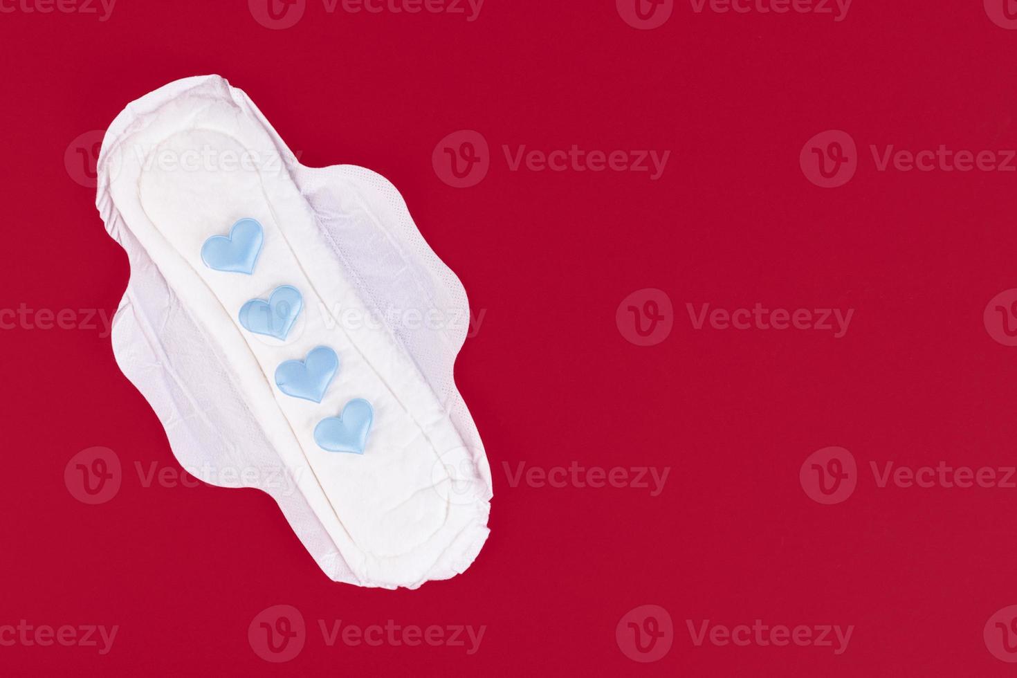 Four blue hearts as a symbol of the menstrual cycle on a feminine sanitary napkin. Feminine hygiene products during the menstrual cycle. Red background. Copy space. photo