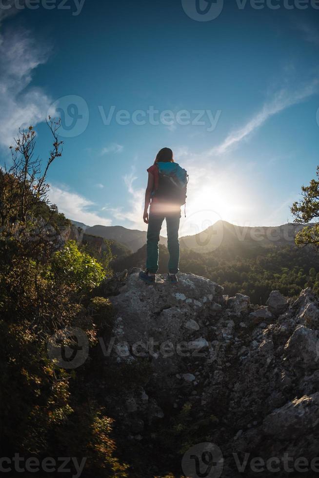 The silhouette of a woman with a backpack against the backdrop of a mountain at sunset photo