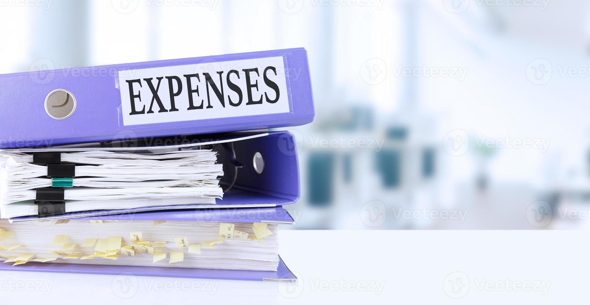 Expenses, text written in a folder with documents in trendy purple color, lying on a stack of papers, documents on an office table, against a background of soft blur office background. photo