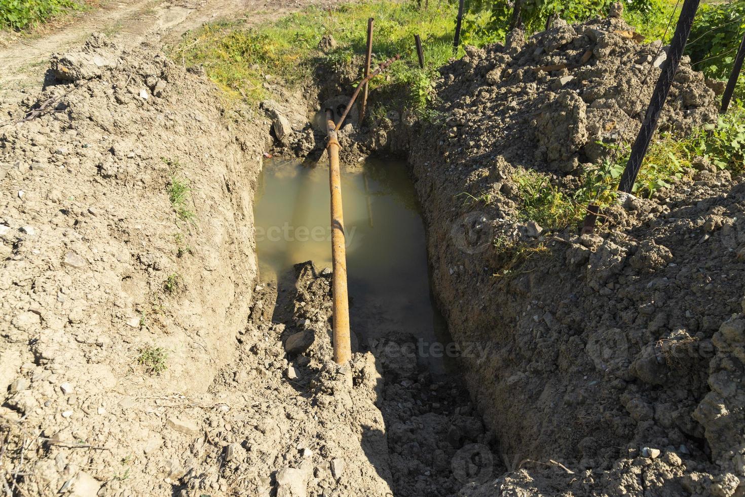 Old rusty metal pipes in a pit with water, water supply system in a mountainous area. Breakthrough of a rusty pipeline. photo