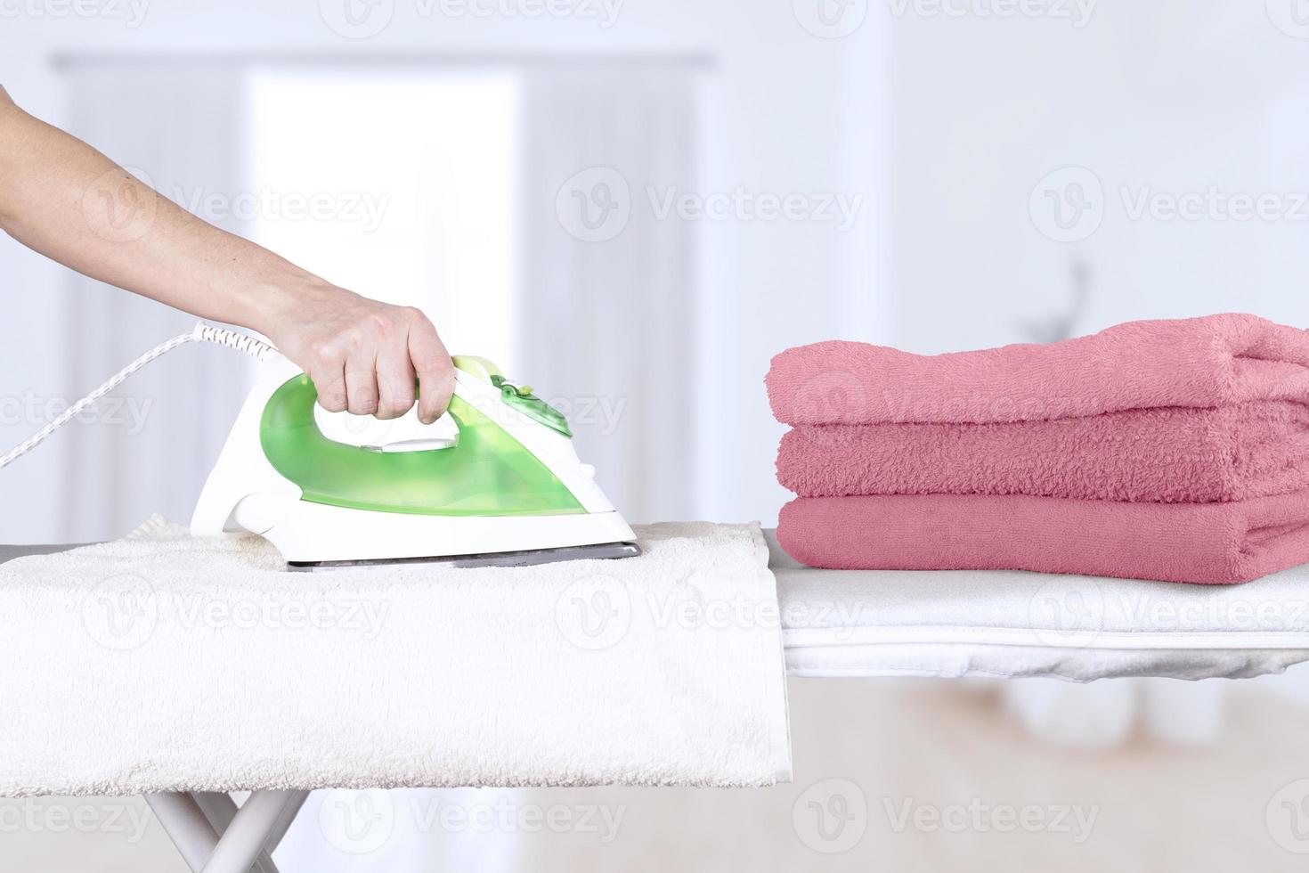 Caucasian woman, wife, mother, housewife, housekeeper, maid ironing bath towels in pink shades, electric iron on ironing board. Home interior background. soft focus. photo