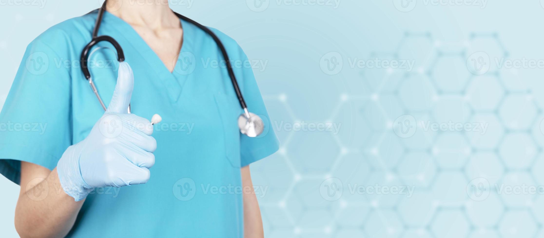 Female Doctor Shows Ok Gesture Or Thumbs Up. Blue medical background. Copy space. photo