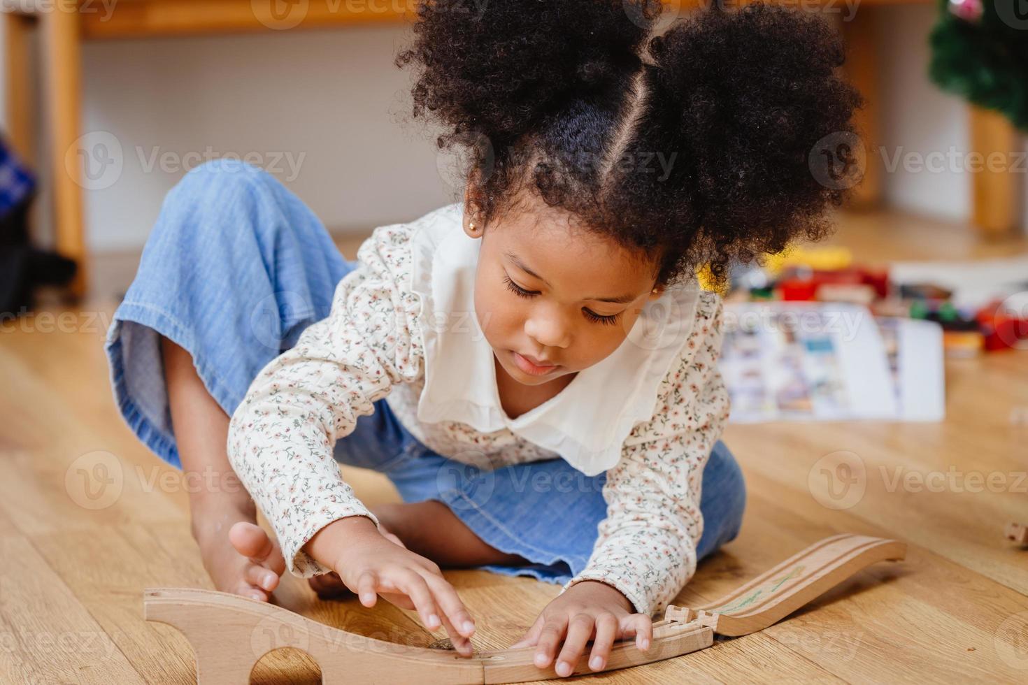 niña pequeña y linda disfruta jugando rompecabezas de madera en el piso de madera en casa en la sala de estar. foto