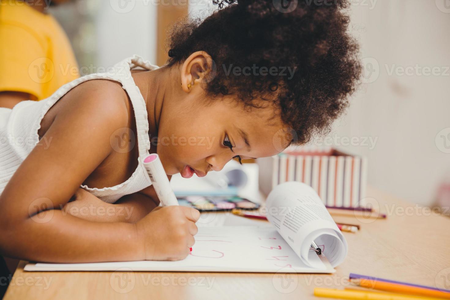 Closeup little child girl black skin writing doing homework at home. photo