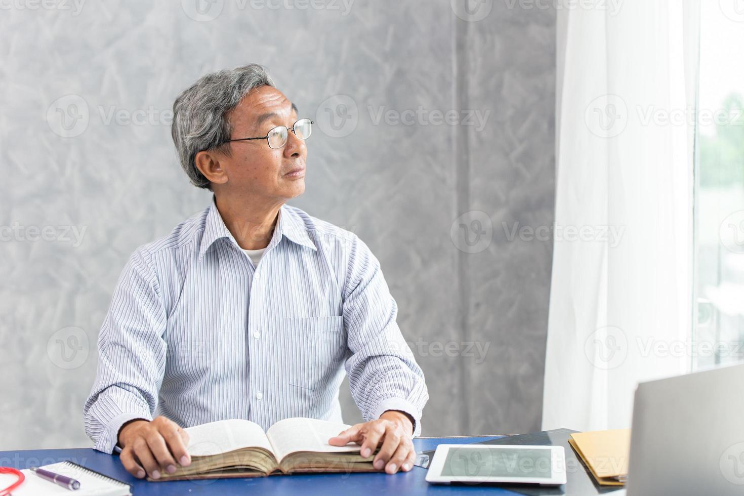 Smart healthy business old man sitting in office, Asian elder thinks looking out of the windows while reading a book. photo