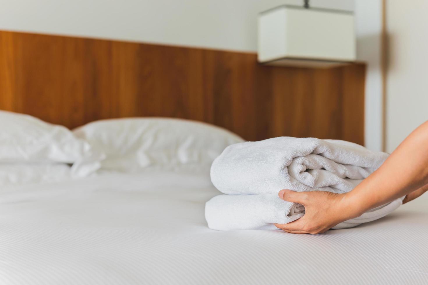 Hands putting fresh white bath towels on the bed sheet. photo