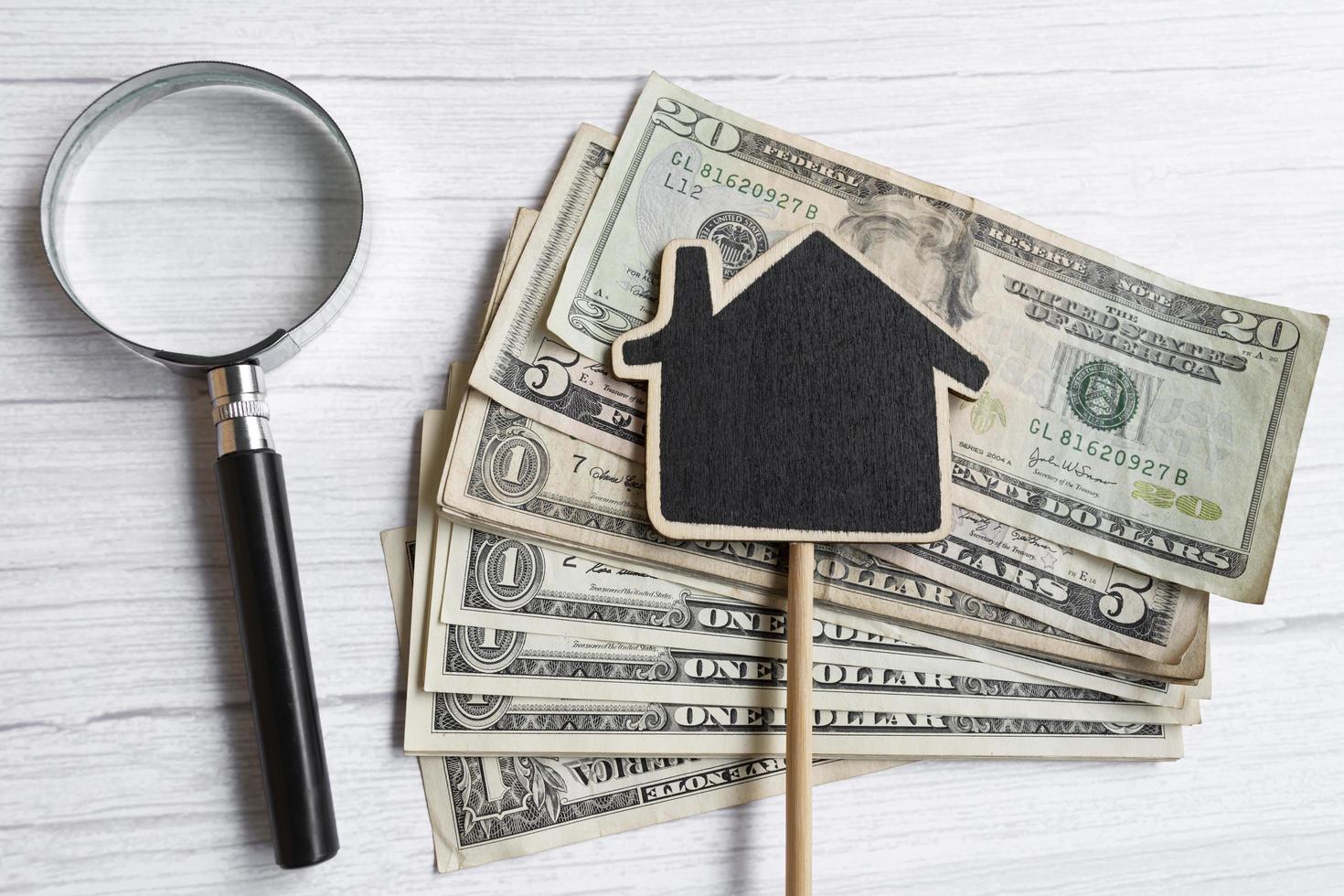 Wooden house model with dollar banknotes and magnifying glass on wooden table photo