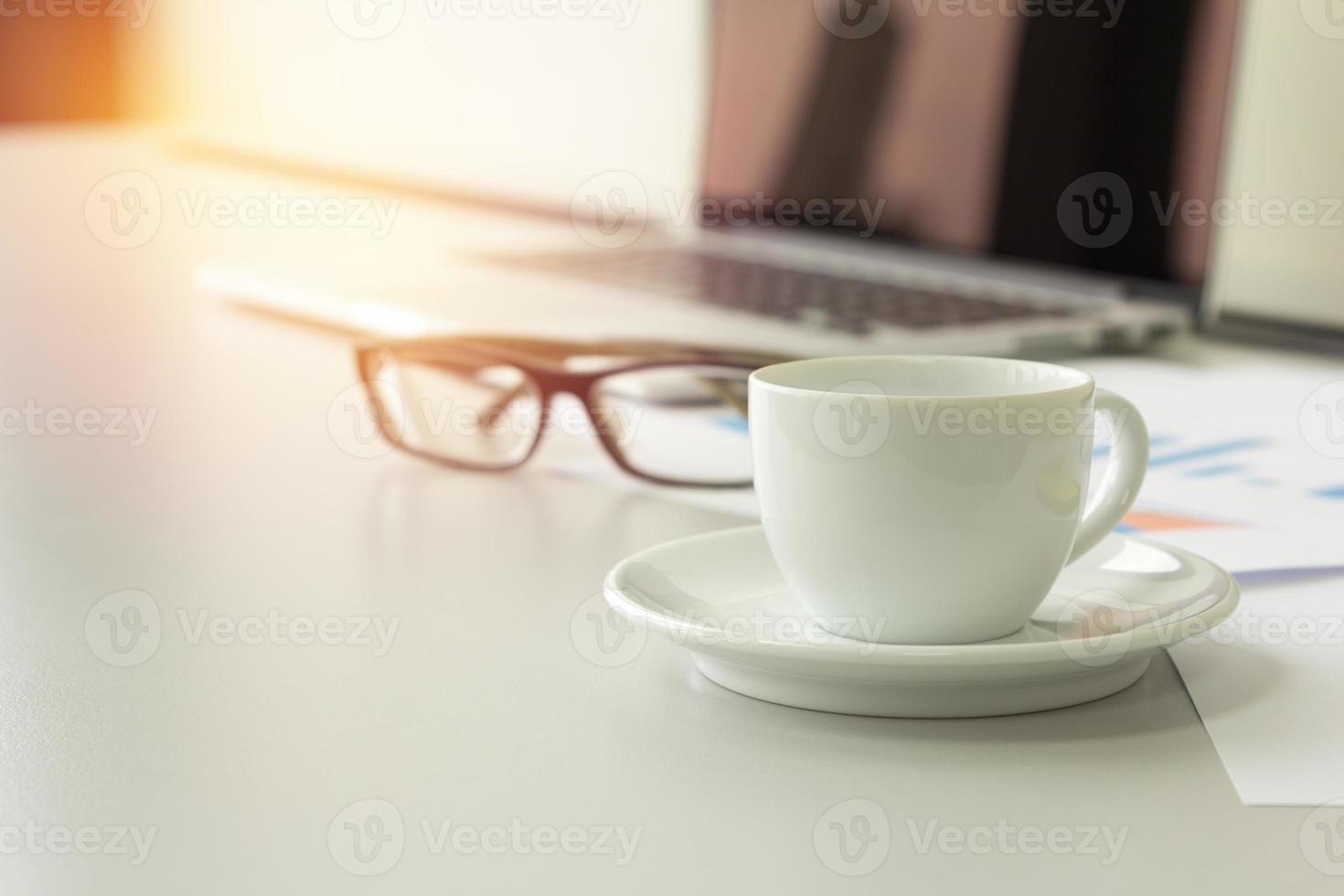 closeup coffee cup on table with laptop, glasses and papers in background, business concept. photo
