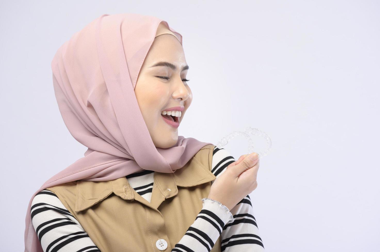 A young muslim woman holding invisalign braces in studio, dental healthcare and Orthodontic concept.. photo