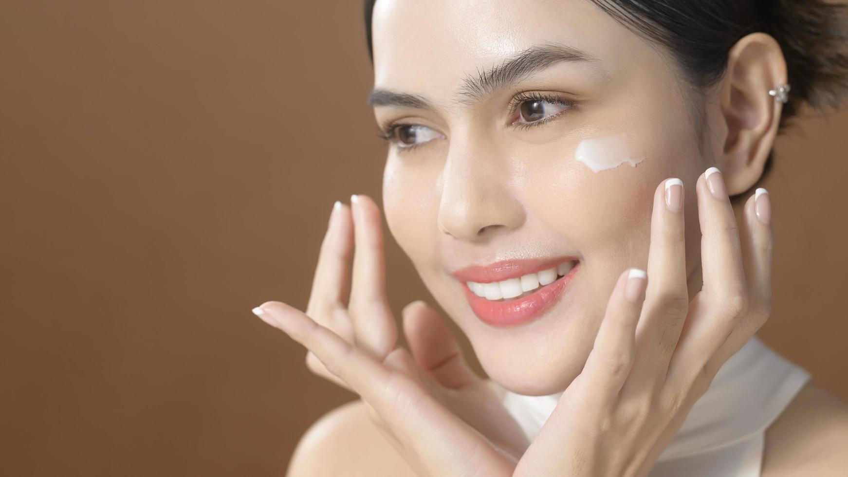 una mujer joven con una cara hermosa está sosteniendo crema, usando crema de su cara, concepto de belleza para el cuidado de la piel foto