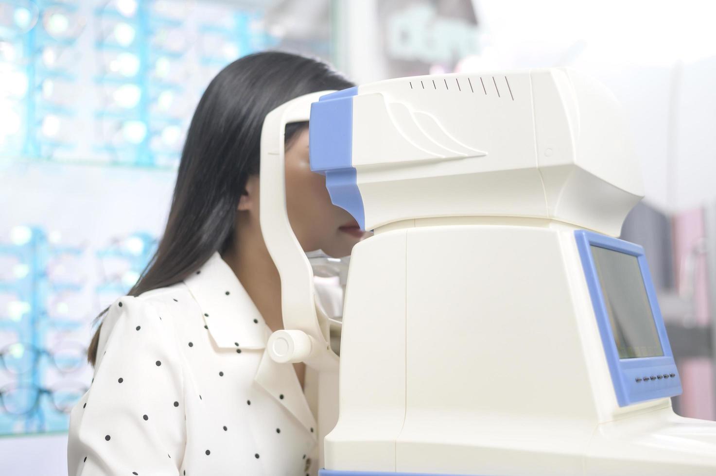 Young female customer being examined visual test using autorefractor by ophthalmologist in optical center, eyecare concept. photo