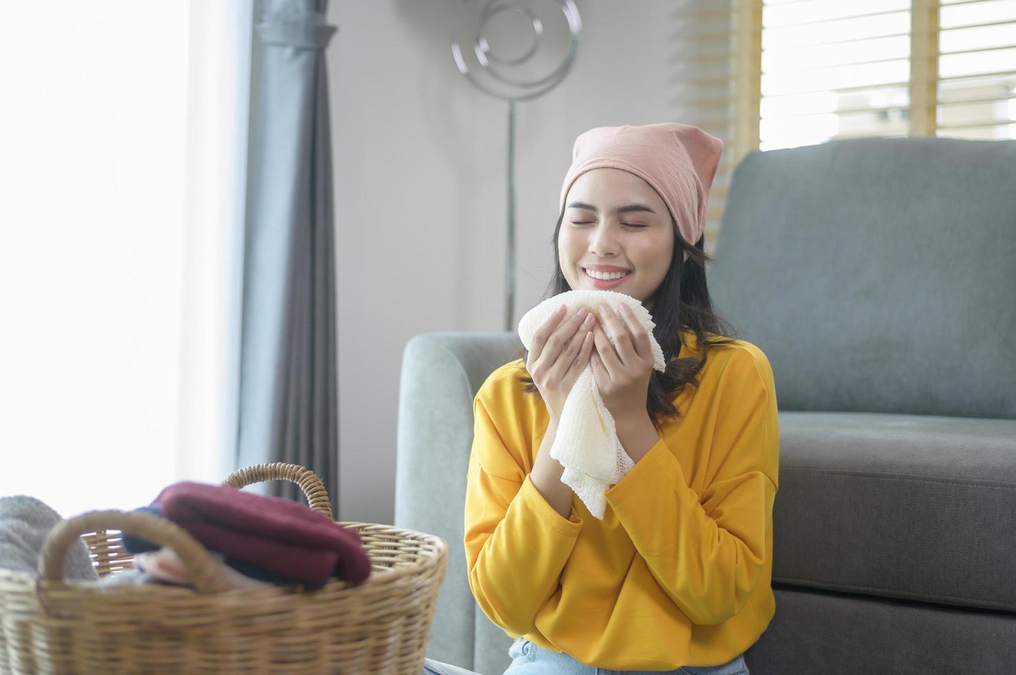 joven mujer feliz con camisa amarilla doblando ropa en la sala de estar, concepto de lavandería foto