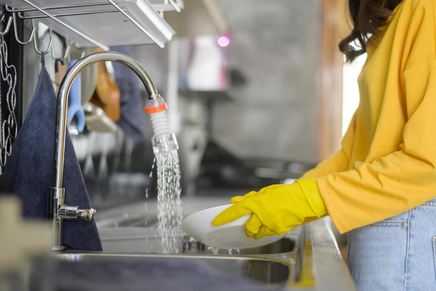 joven mujer feliz usando guantes amarillos lavando platos en la cocina en casa foto