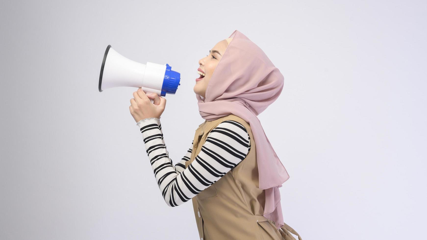 Happy muslim woman is announcing with megaphone on white background photo