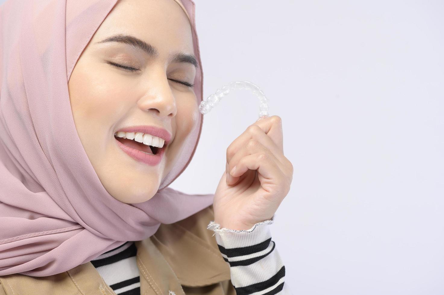 A young muslim woman holding invisalign braces in studio, dental healthcare and Orthodontic concept.. photo