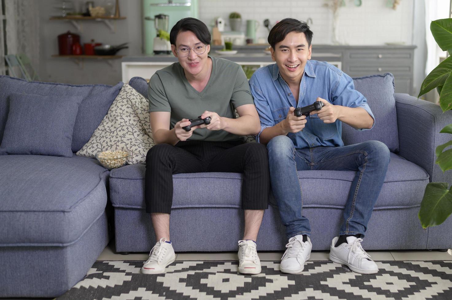 joven pareja gay sonriente jugando videojuegos en la sala de estar en casa, lgbtq y diversidad foto