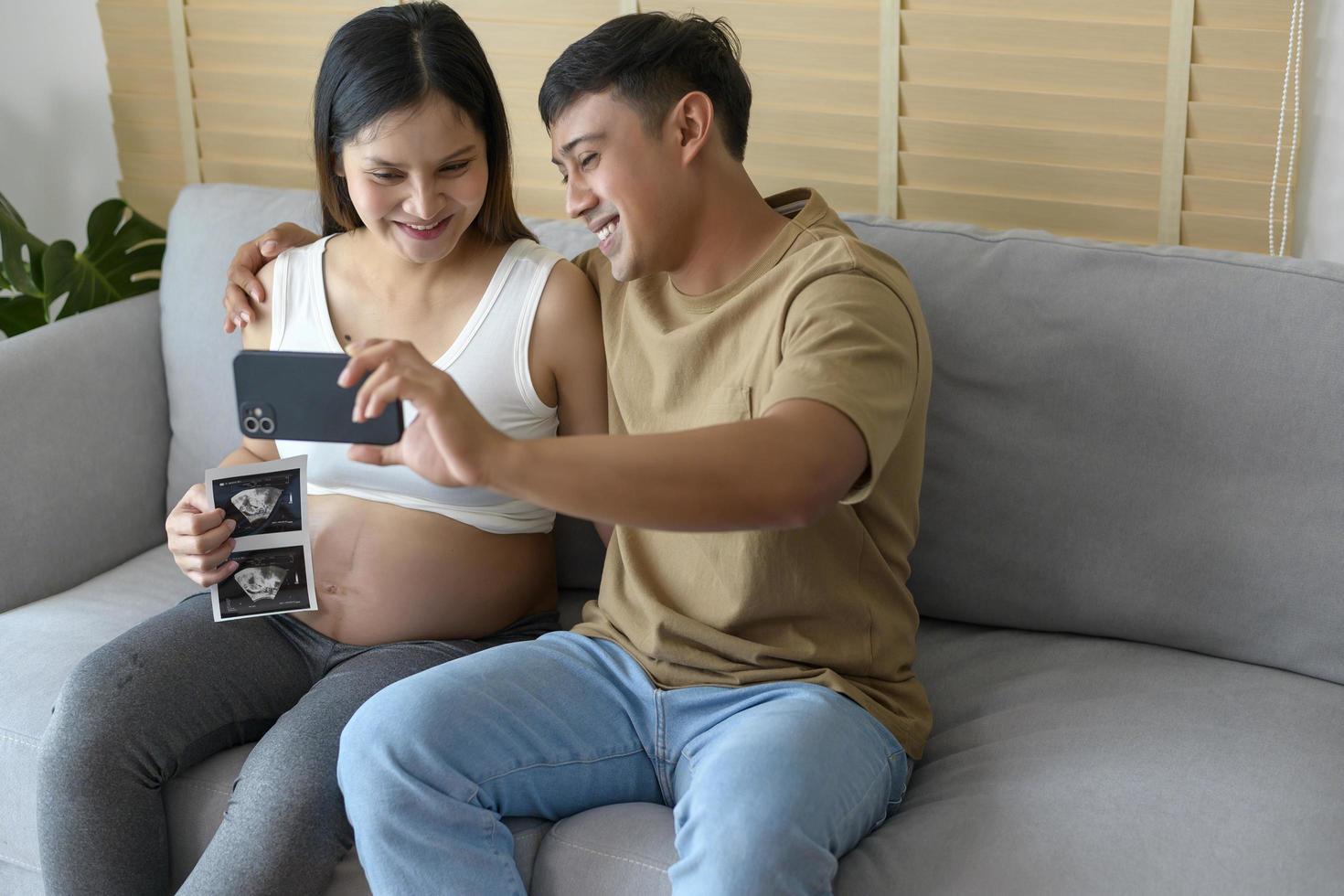 Young pregnant woman with husband embracing and video call with family and friends by smartphone on social media, family and pregnancy care concept photo
