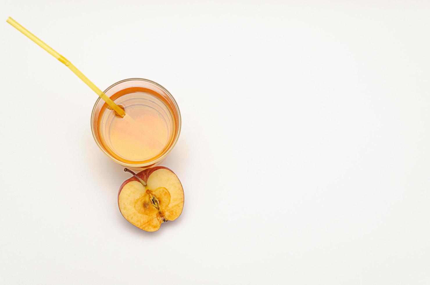 a glass of apple juice with a straw and half a red apple on a white background photo
