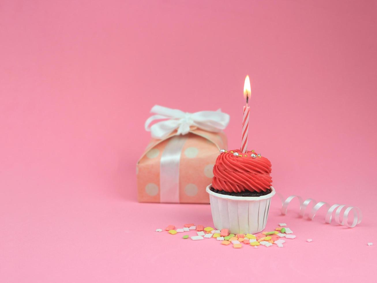 Sweet red cupcake with bow candle and gift box on pink background with copy space. Happy birthday party background concept. photo