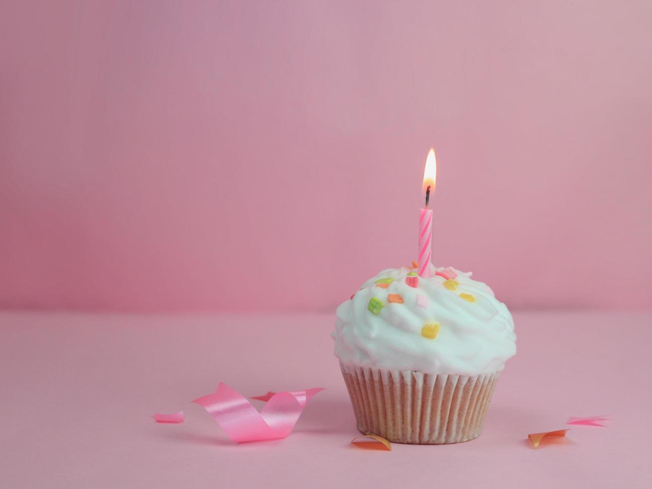 cupcake de feliz cumpleaños y vela de arco sobre fondo rosa con espacio de copia. foto