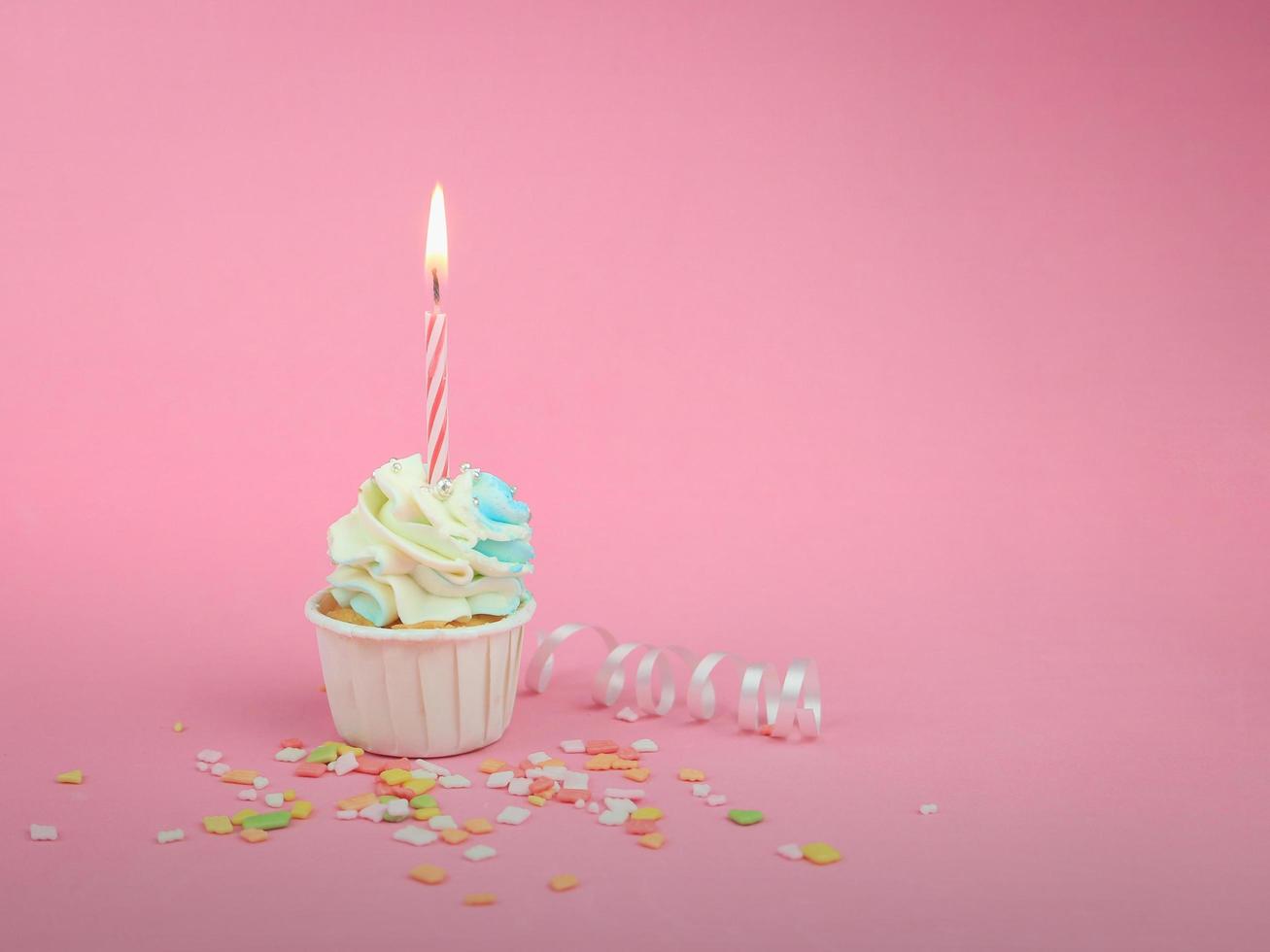 Sweet cupcake with bow candle on pink background with copy space. Happy birthday party background concept. photo